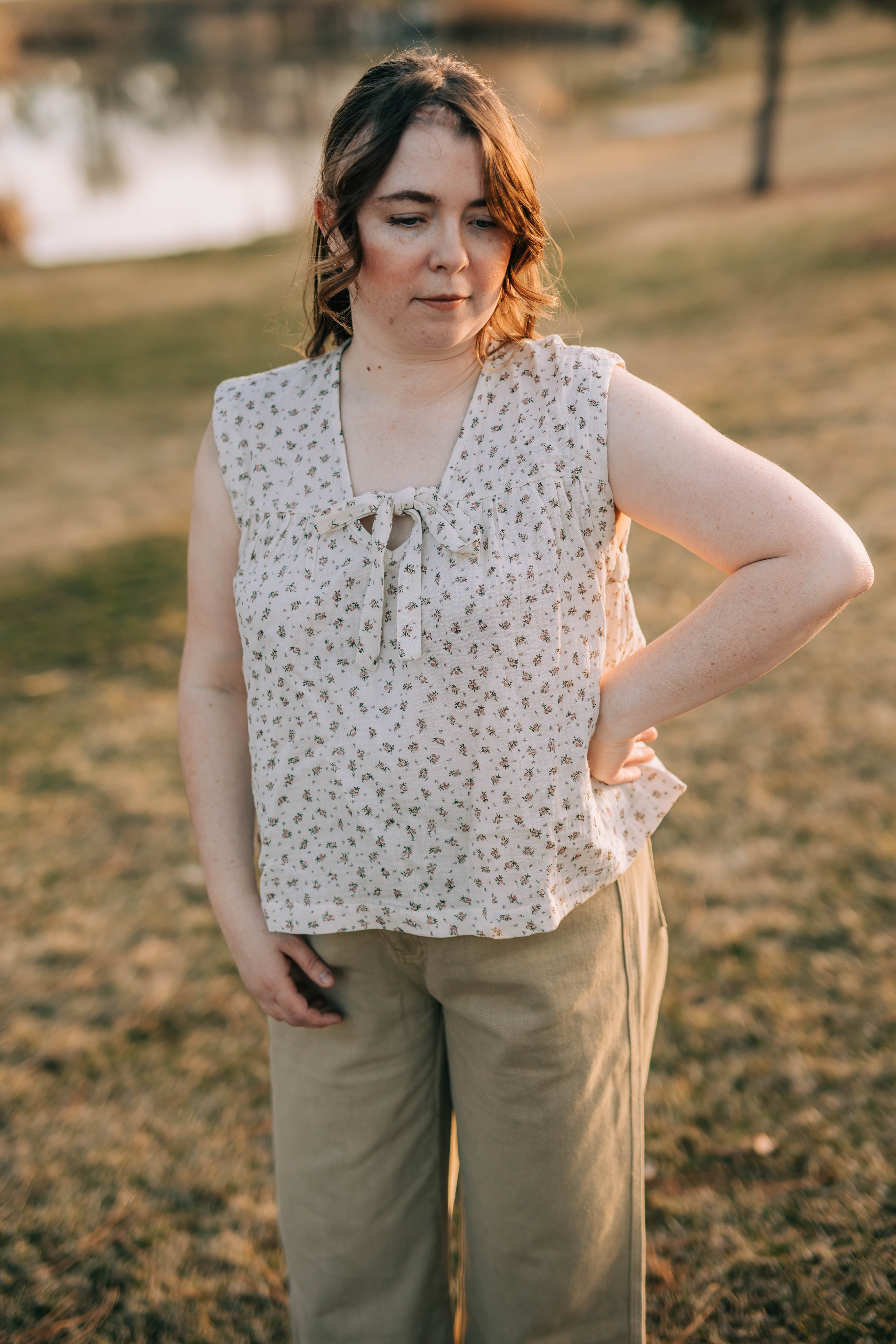 Bethany stands on a hill with hand on hip. She is wearing the Molly top which is a 100% cotton, cap sleeve top. The Molly top is cream with a small pink floral print.